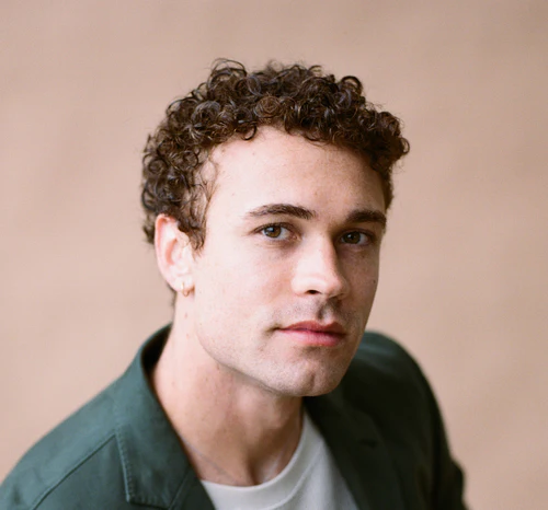 Man in a green jacket looking at camera against a beige background